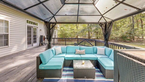 A covered outdoor seating area with a sectional sofa and two side tables, overlooking a wooded area. - Dog-friendly Family Retreat Near Chincoteague Bay! (Greenbackville)