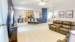 A spacious living area with a leather sofa, a dining table with chairs, a kitchen area with wooden cabinets, and a ceiling fan. - Dog-friendly Family Retreat Near Chincoteague Bay! (Greenbackville)