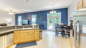 A modern kitchen with wooden cabinets, a stainless steel refrigerator, and a dining area with a table and chairs. - Dog-friendly Family Retreat Near Chincoteague Bay! (Greenbackville)
