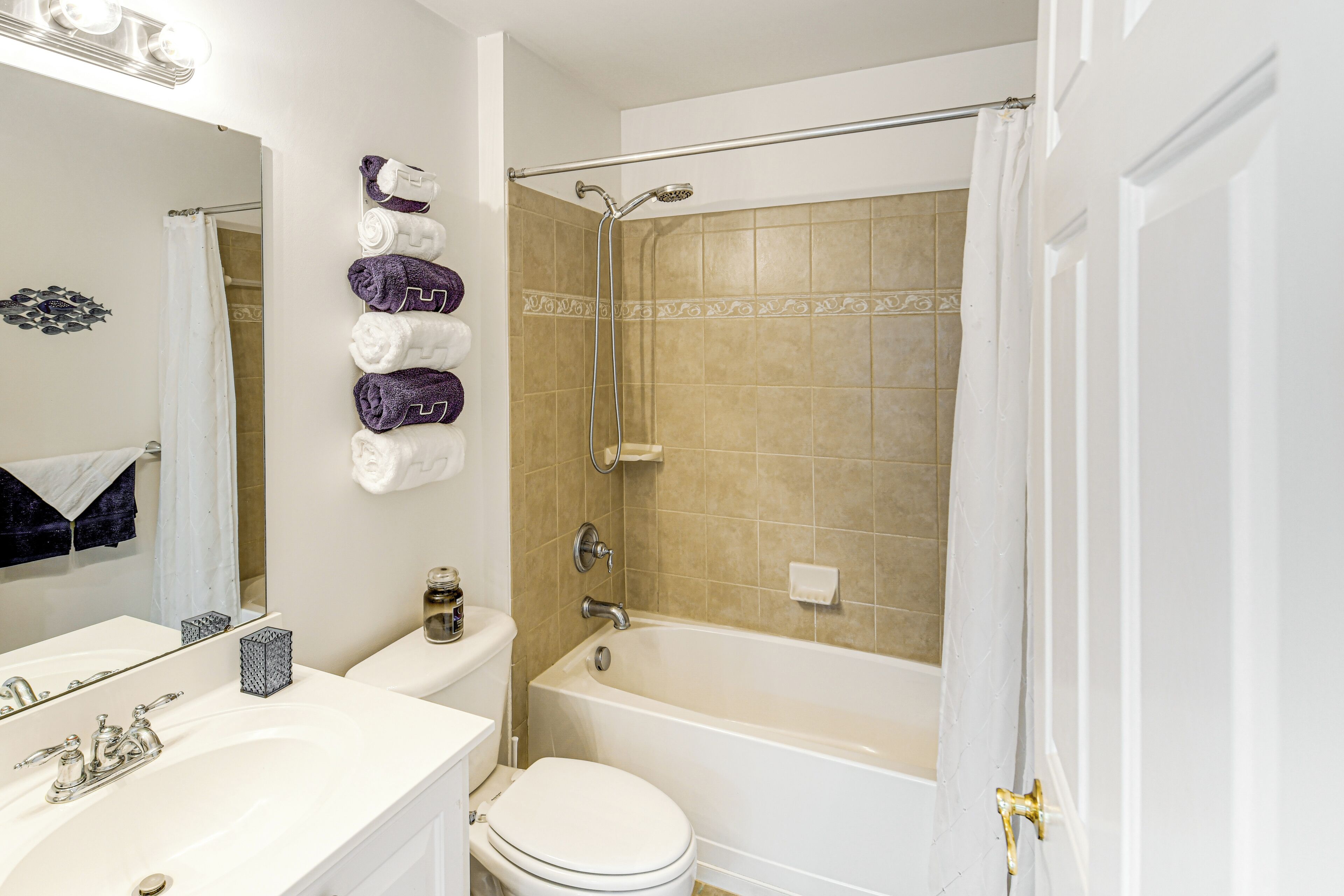 Une salle de bain avec un lavabo, des toilettes et une baignoire, tous de couleur blanche. Des serviettes sont accrochées au mur et il y a un rideau de douche.