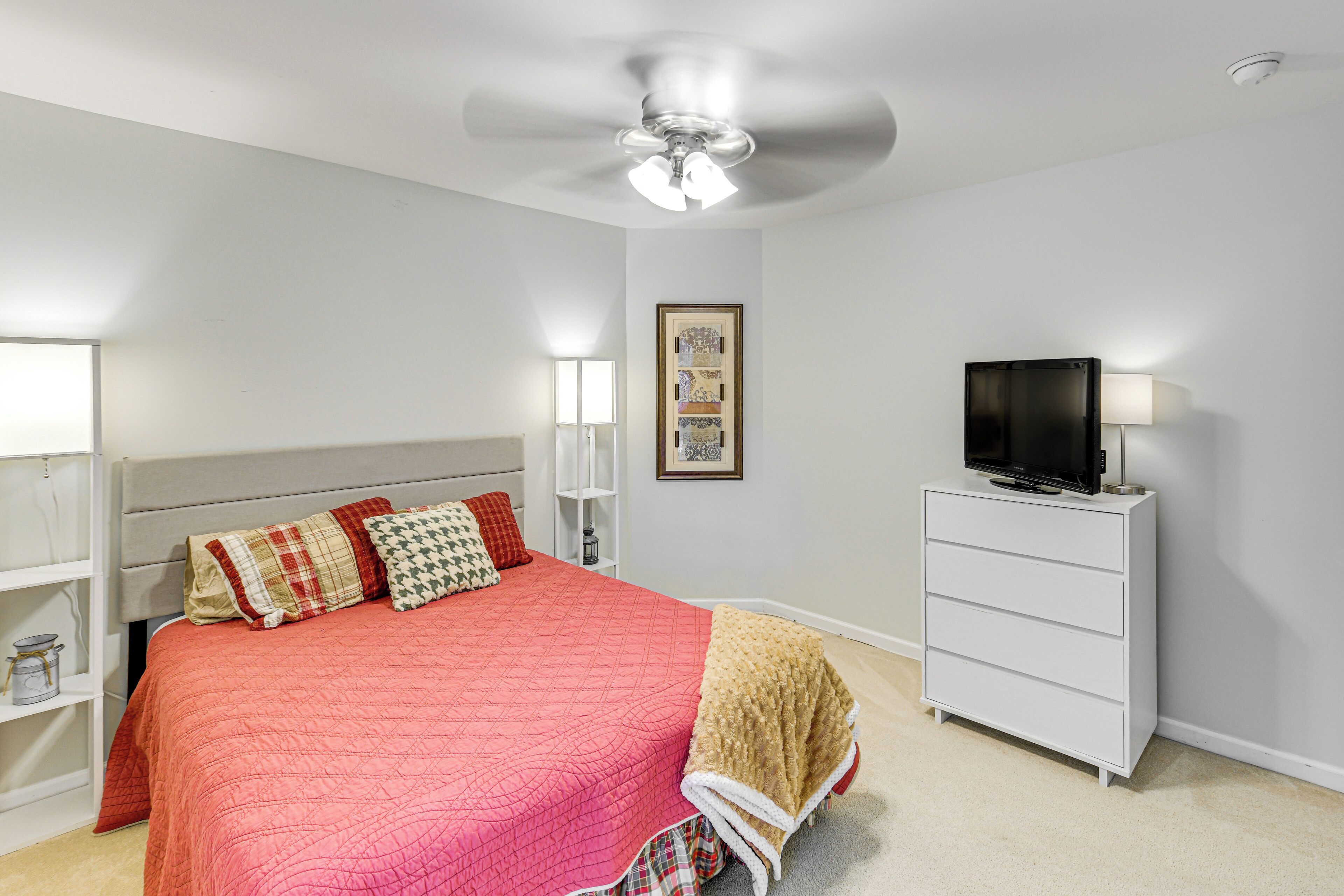 A bedroom with a bed, a ceiling fan, a TV on a dresser, and a framed picture on the wall.