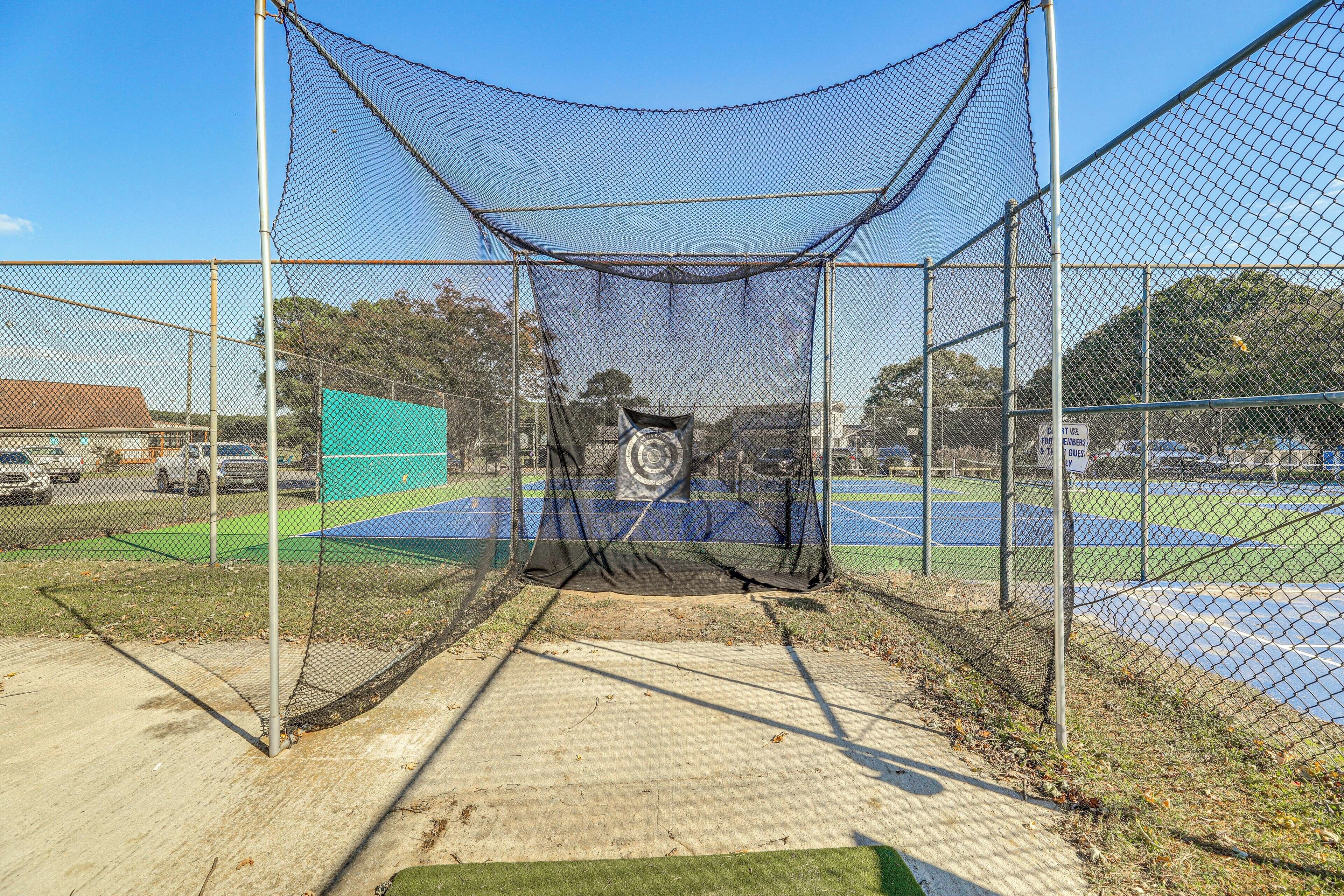 A baseball batting cage with a netted structure, a concrete floor, and a blue field in the background.