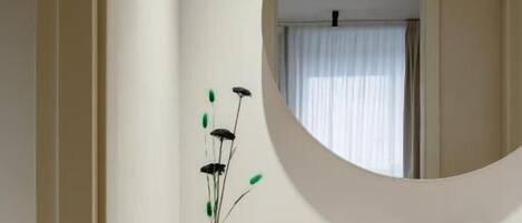 Een badkamer met een ronde spiegel, een witte wastafel en een vaas met bloemen.