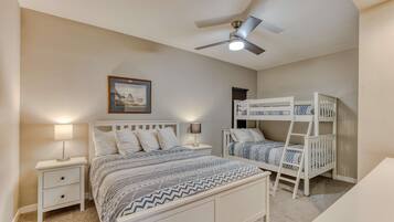 Une chambre avec un lit simple, un lit superposé, une table de chevet avec une lampe, un ventilateur de plafond et un tableau encadré au mur.