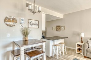 A kitchen with a wooden table, bar stools, and a hanging light fixture. - Sand & Sea (110) Pacific Nook: Oceanview & Pool (Seaside)