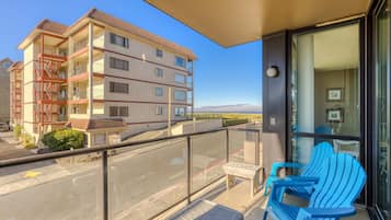 Een balkon met blauwe Adirondack stoelen, een helder uitzicht op een meerlaags gebouw en een verafgelegen landschap.