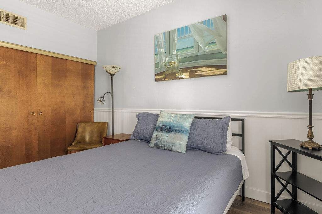 Une chambre à coucher avec un lit, une armoire, une chaise, une lampe et un tableau accroché au mur.