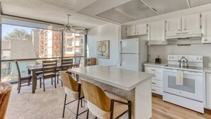 Een moderne keuken met witte kasten, een groot kookeiland met barstoelen, een inbouwoven en een uitzicht door grote ramen.
