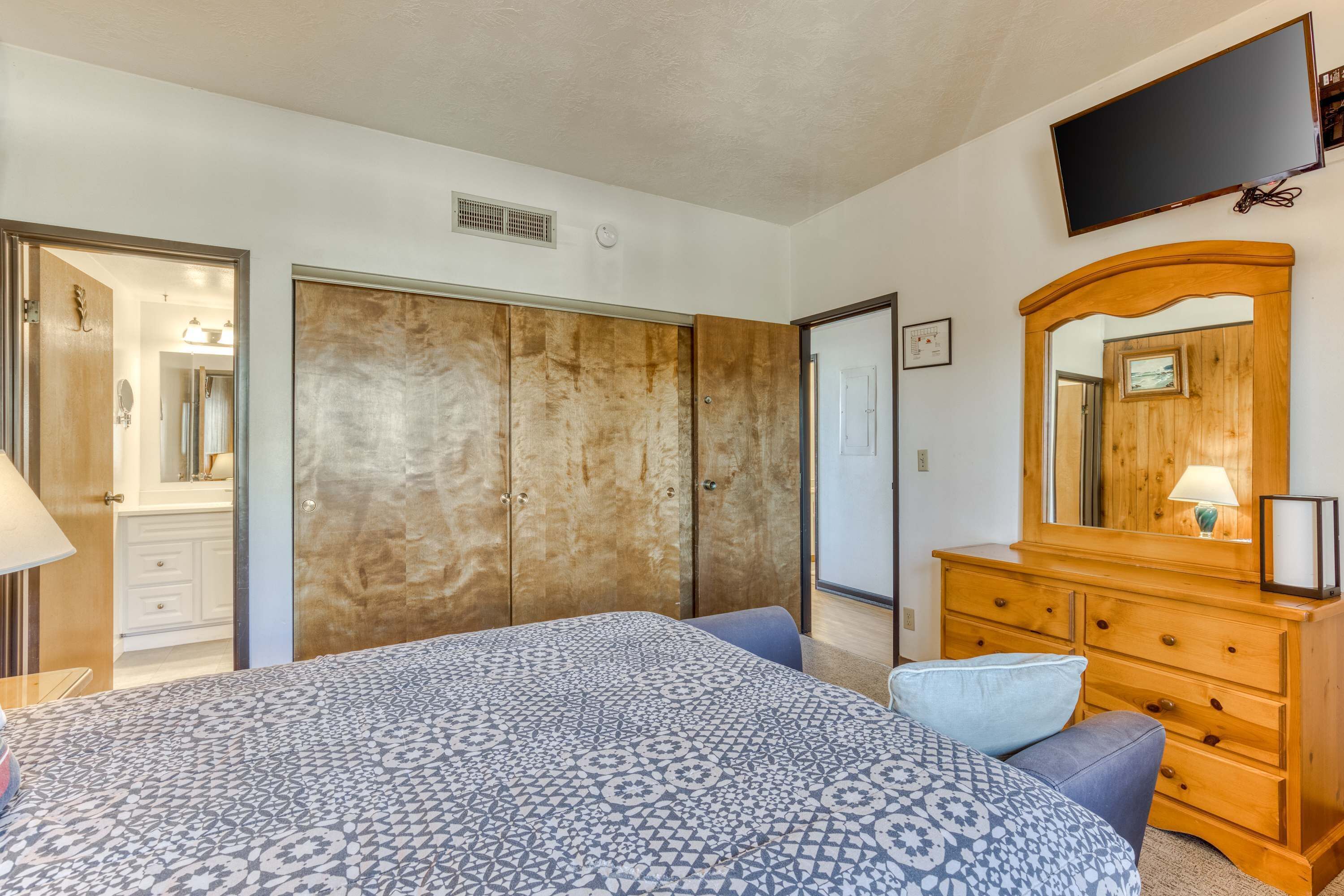 Un dormitorio con una cama grande, un aparador de madera, un espejo y un televisor montado en la pared.