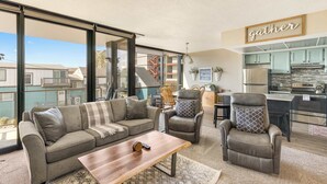 A spacious living area with a sofa, chairs, a coffee table, and a kitchen in the background. - Sand & Sea (118) Shore Thing - Oceanside Charm (Seaside)
