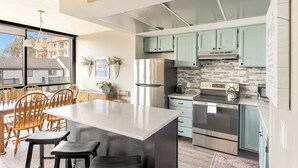 A modern kitchen with a central island, stainless steel appliances, and light green cabinets. - Sand & Sea (118) Shore Thing - Oceanside Charm (Seaside)