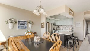 A modern kitchen with light blue cabinets, a stainless steel refrigerator, and a central island with stools. - Sand & Sea (118) Shore Thing - Oceanside Charm (Seaside)