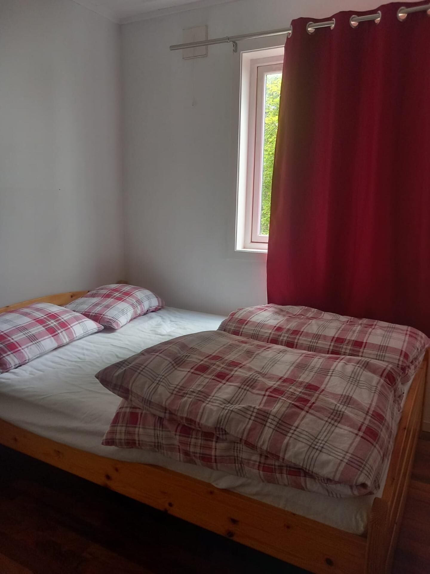 A single bed with plaid bedding and a window with a red curtain.