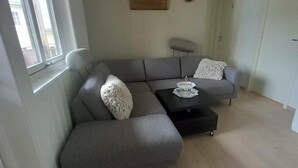 A modern living room with a grey sectional sofa, a small side table, and a painting on the wall. - Arctic Paradise - 4 Bedroom Apartment in Tromso (Tromsø)