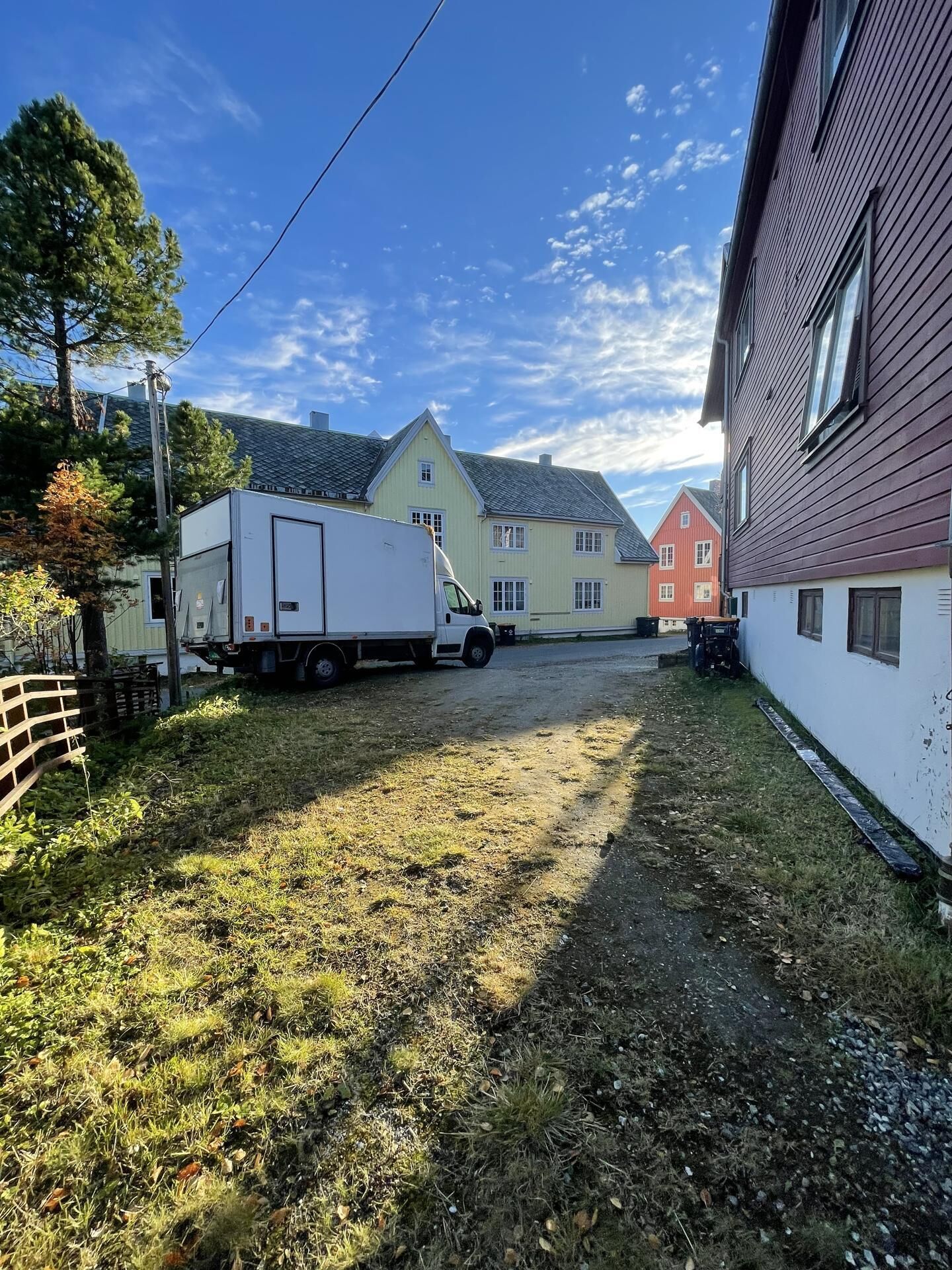 Un quartier résidentiel avec un camion blanc garé, une pelouse verdoyante et des maisons aux façades de couleurs différentes.