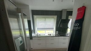 A narrow kitchen with a refrigerator, a window with blinds, a countertop with kitchen appliances, and a rug on the floor. - Arctic Paradise - 4 Bedroom Apartment in Tromso (Tromsø)