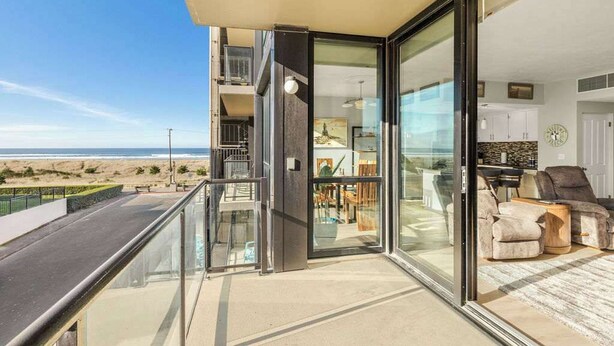 Een modern appartement met een glazen balkon met uitzicht op een strand.