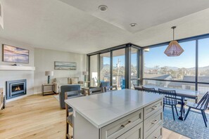 A spacious living area with a fireplace, a dining table, and a large window offering a city view.