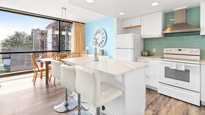 A modern kitchen with a central island, white cabinetry, and a view of the outside. - Sand & Sea (214) Turtle Cove - Condo on the Prom w Pool (Seaside)