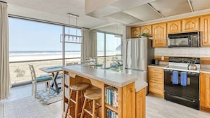 Una cocina con armarios de madera, un refrigerador de acero inoxidable, un microondas y una estufa. Hay un ventanal con vistas a la playa.