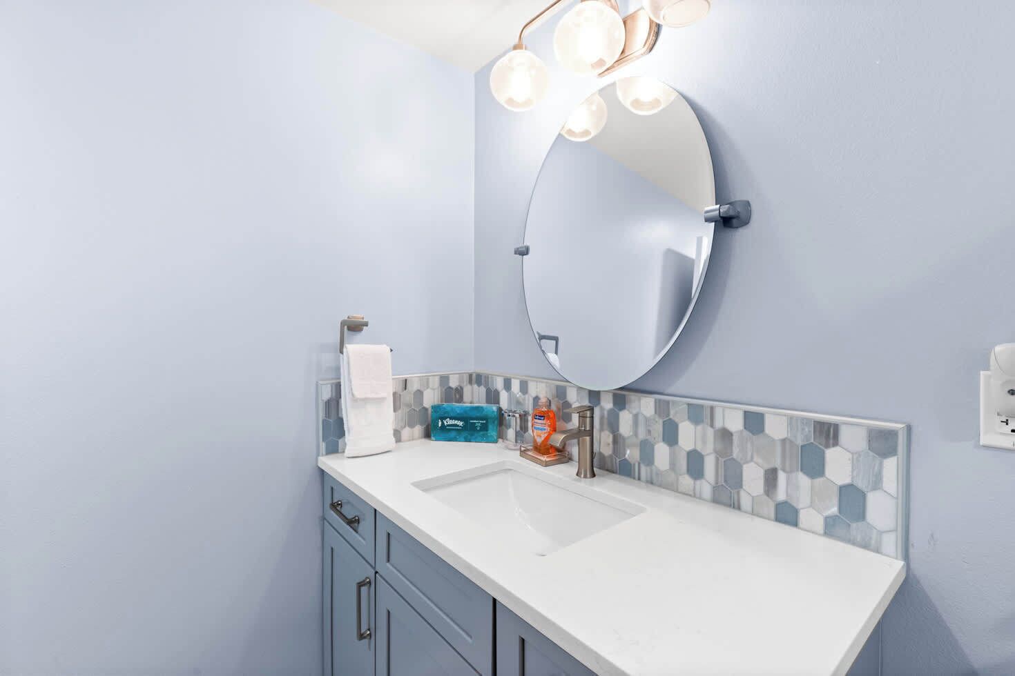 A bathroom with a white sink, a round mirror, and a towel rack.