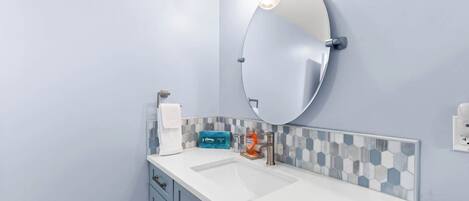 A bathroom with a white sink, a round mirror, and a towel rack.