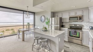 A modern kitchen with a large island, stainless steel appliances, and a view of the beach. - Sand & Sea (306) Sojourn - Oceanfront luxury (Seaside)