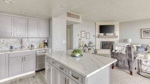 A modern kitchen with grey cabinets, a marble island, and a fireplace in the living area. - Sand & Sea (306) Sojourn - Oceanfront luxury (Seaside)
