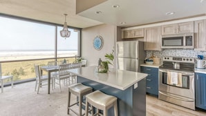 Een moderne keuken met een groot eiland, roestvrijstalen apparatuur en uitzicht op het strand.
