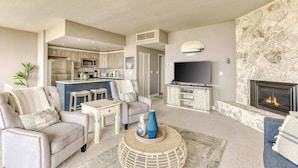 Een moderne woonkamer met een open haard, een televisie en een keuken op de achtergrond.