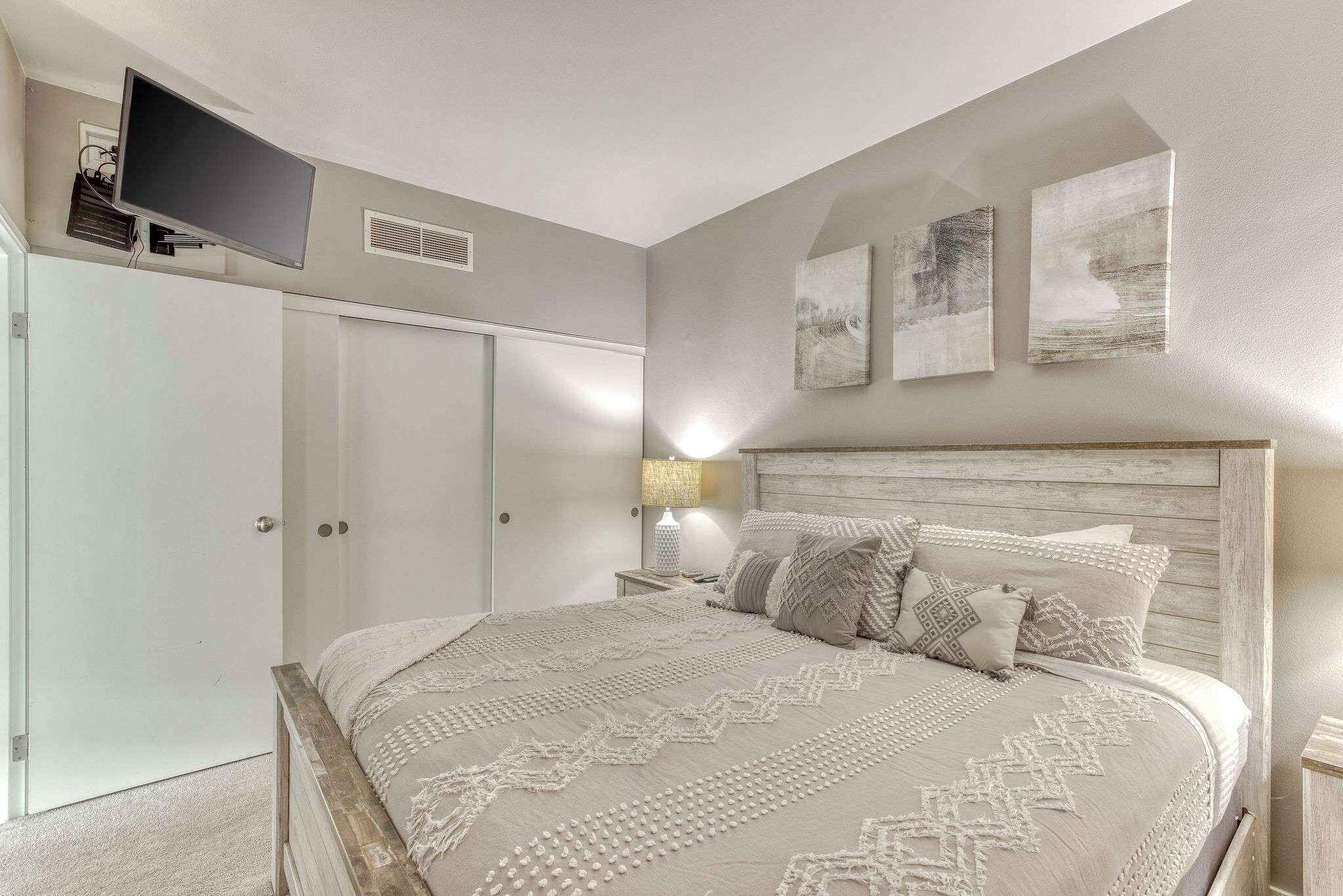 A bedroom with a bed, a TV mounted on the wall, and artwork on the wall.