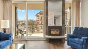 A living room with a fireplace, two blue sofas, a glass coffee table, and a sliding glass door leading to an outdoor balcony. - Sand & Sea (310) Driftwood - Oceanfront Pet Friendly (Seaside)