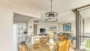A modern kitchen with white cabinets, a dining area with a glass table, and a living room with a sofa and a TV.