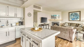 A modern kitchen with white cabinets, a central island, and a dining area with a sofa and fireplace.
