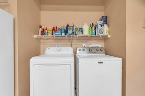 A laundry area with two front-loading washing machines and a shelf above containing various cleaning products. - Pet-Friendly Home 4 Miles to Beach & Shops (Naples)