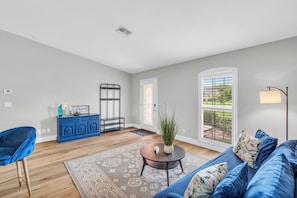 A spacious living room with a blue sofa, a coffee table with a plant, a blue cabinet, and a large window with a view of greenery. - Pet-Friendly Home 4 Miles to Beach & Shops (Naples)