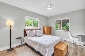 Un dormitorio con cama, lámpara de noche, cómoda, silla y ventana con vista a zonas verdes.
