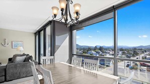 Ein modernes Wohnzimmer mit Essbereich, großen Fenstern und Blick auf eine Stadt und Berge.