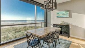 A dining area with a large table and chairs, a desk with a computer, and a painting on the wall. - Sand & Sea (508) Salt Life - Lux Beachfront w Pool (Seaside)