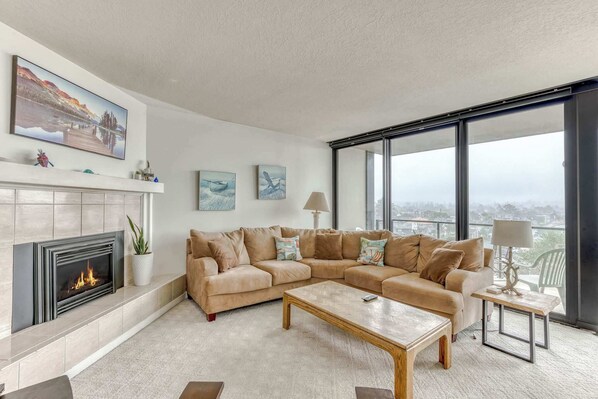 Ein modernes Wohnzimmer mit Kamin, großzügigem Ecksofa, Couchtisch und großen Fenstern mit Blick auf die Stadt.