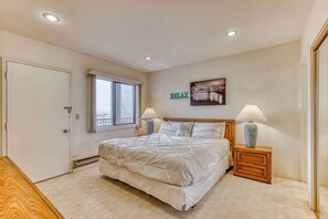 Ein Schlafzimmer mit einem Bett, zwei Nachttischlampen, einem Fenster, einer Tür und einem an der Wand hängenden Kunstwerk.