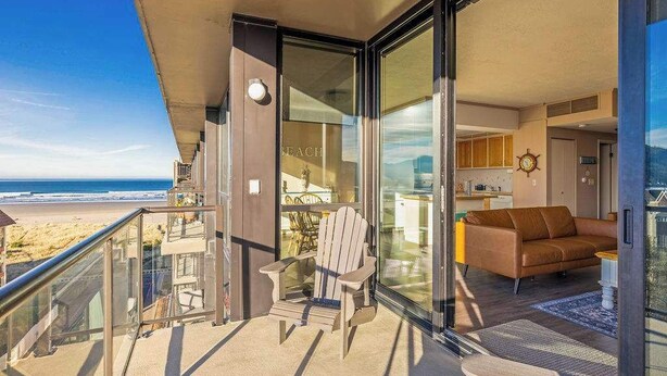 A balcony with a view of the beach, a wooden chair, and a brown sofa. - Sand & Sea (618) Seaside Panorama -Cozy Beachfront (Seaside)