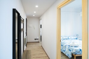 Un pasillo estrecho que conduce a un dormitorio con cama y mesita de noche.