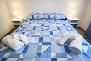 A neatly made bed with a geometric patterned bedspread, two white towels, and two bedside lamps on nightstands. - Lupo di Mare by Wonderful Italy (Savona)