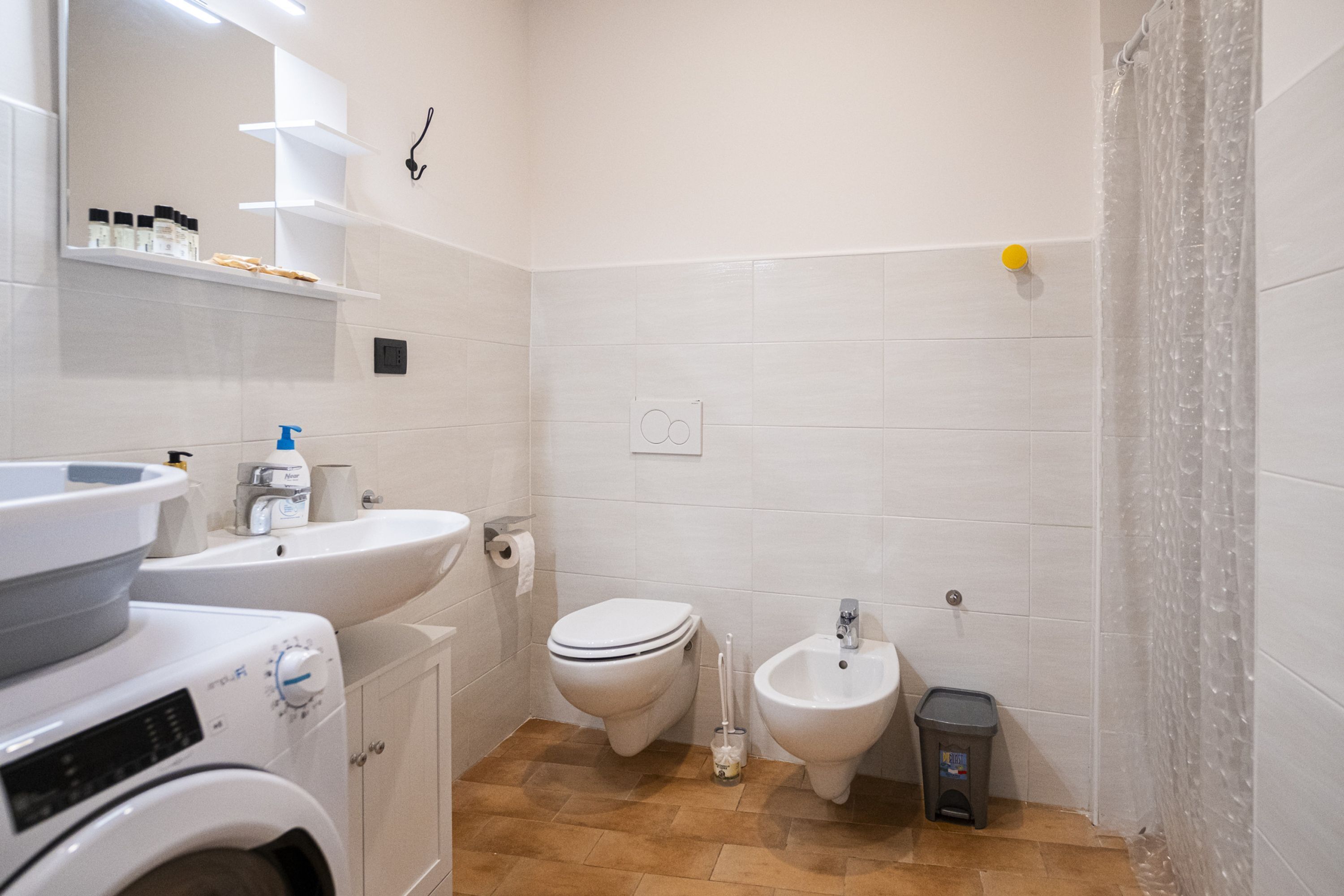 A bathroom with a washing machine, sink, toilet, bidet, and a shower curtain.