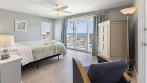 Un dormitorio con cama, escritorio, silla, ventilador de techo y vista al mar.