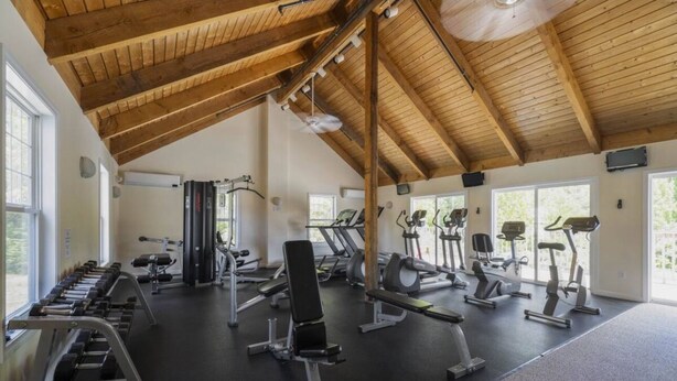 Un gimnasio con diverso equipo de ejercicio, ventanas amplias y techo de madera.
