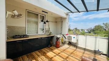 A compact balcony with a wooden floor, a small kitchen area with a gas stove, a water heater, and a red gas cylinder.