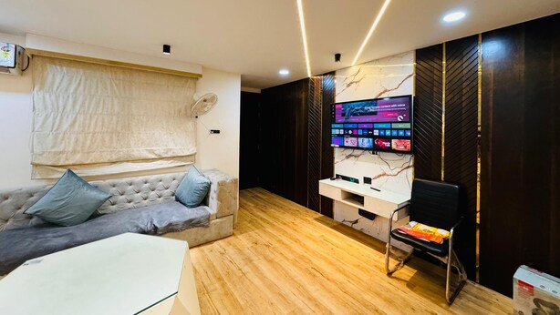 Una habitación moderna con sofá, escritorio y televisor grande montado en la pared.