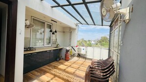 Un balcón con piso de madera, un tanque de gas, un ventilador y vistas de la ciudad.